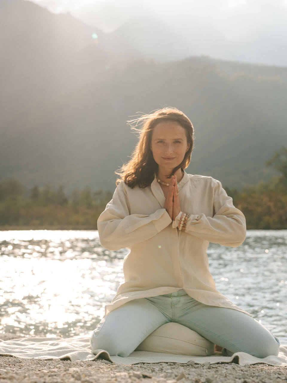 Meditationslehrerin, Meditationscoach in Meditationspose auf Meditationskissen vor See